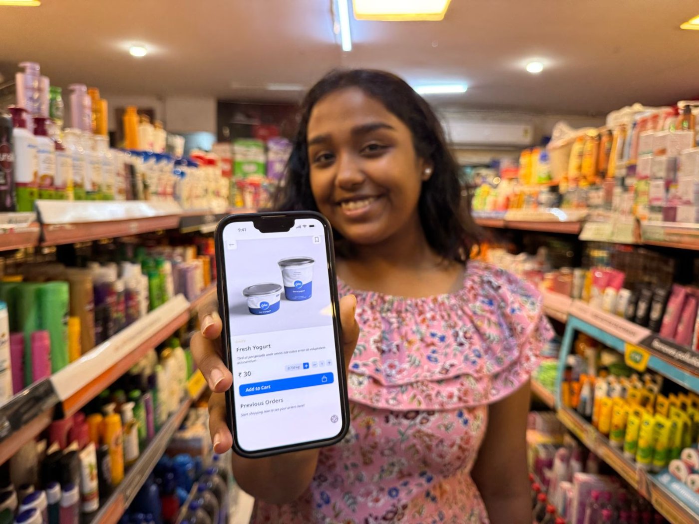 A smiling shopper holding a phone showing the Grab & Go product screen inside a real store